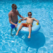 A child floating in a swimming pool using a blue and yellow inflatable tube while his father helps him.