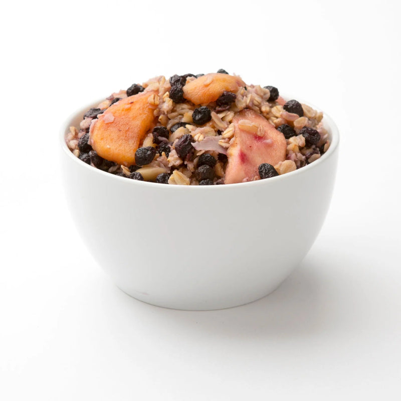 Picture of a white bowl filled to the brim with yummy looking oatmeal and fruit against a white background. 