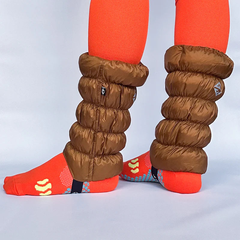 Side view of a model in orange socks wearing a pair of light brown gaiters against a white background. 