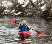 Woman in a red kayak paddling down a stream in the winter.