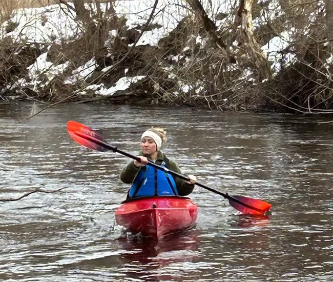 Woman in a red kayak paddling down a stream in the winter.