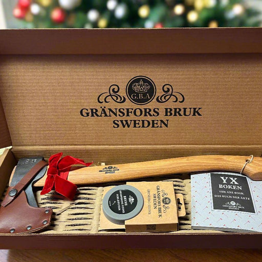 A Gransfors Bruk Small Forest Axe, with a sharpening stone and a copy of The Axe Book, neatly arranged and presented in a gift box with a red bow.