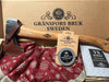 A Gransfors Bruk Small Forest Axe, Sharpening stone, and a copy of The Axe Book propped up with a festive fabric featuring gold snowflakes on a red linen background, with the Gransfors Bruk Sweden logo imprinted on the inside of the gift box lid. Fabric not included.