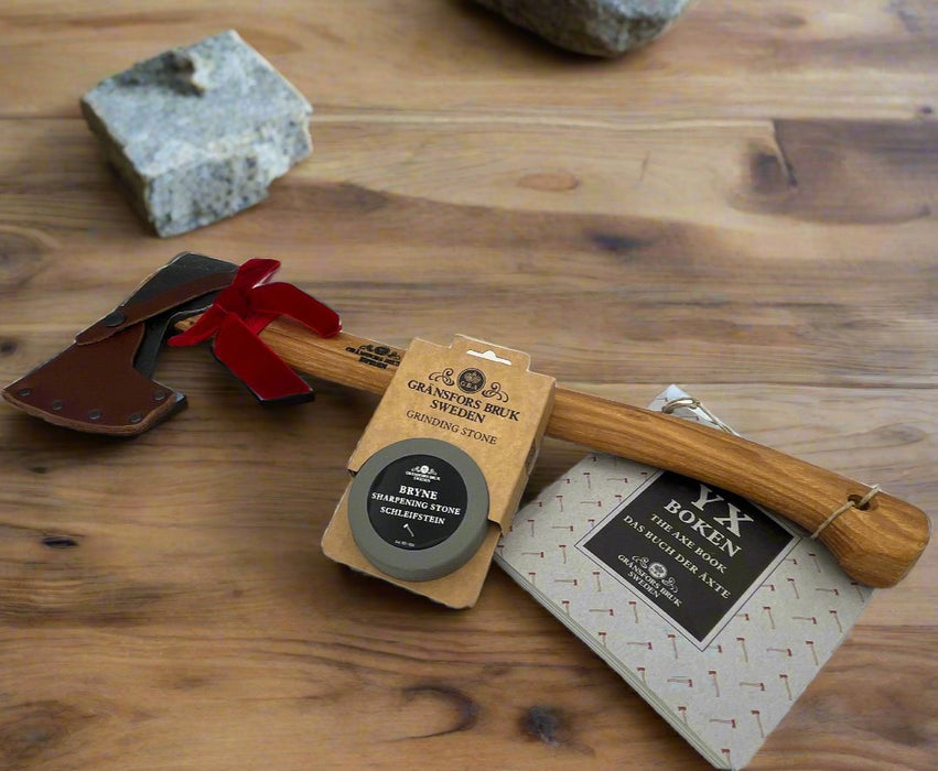 A Gransfors Bruk Small Forest Axe, sharpening stone, and a copy of The Axe Book sit on a wooden work bench.