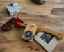 A Gransfors Bruk Small Forest Axe, sharpening stone, and a copy of The Axe Book sit on a wooden work bench.