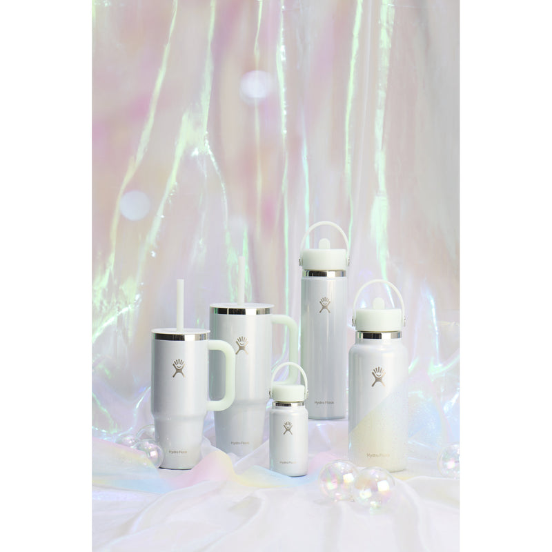A set of white insulated water bottles and tumblers with silver metal accents and a small logo, arranged on a white surface with iridescent hanging fabric in the background.