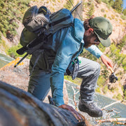 Person with a backpack and fishing gear crossing a stream in a natural setting