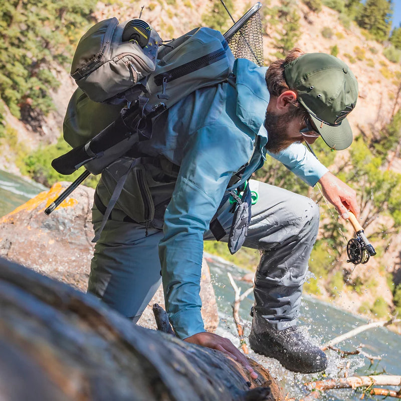 Person with a backpack and fishing gear crossing a stream in a natural setting
