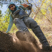 Man in chest waders and wading boots climbing on a riverbank