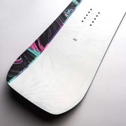 Close up of a white snowboard with black, blue, and pink accents against a gray background. 