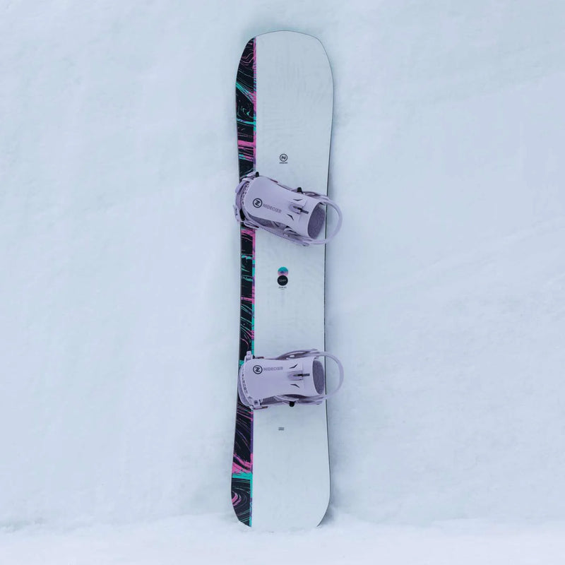 White snowboard with black accents and pink bindings on a snowy hill. 