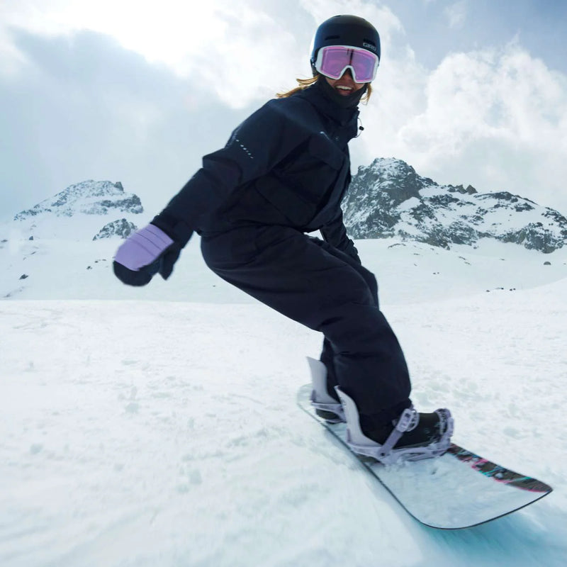 Woman riding a white snowboard with black accents down a snowy mountain.