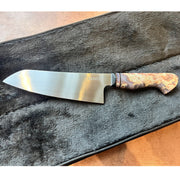 A chef's knife with a satin-finished steel blade and a marbled wood handle, displayed diagonally on a dark gray plush zippered case over a brown surface.