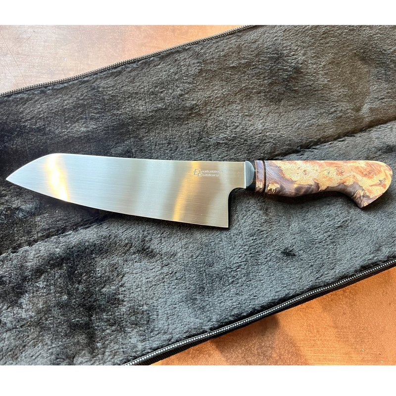 A chef's knife with a satin-finished steel blade and a marbled wood handle, displayed diagonally on a dark gray plush zippered case over a brown surface.