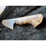 A chef's knife with a polished steel blade and an ornate, swirling wood-grain handle in brown, gold, and black tones, resting on a dark textured surface.