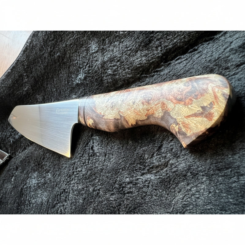 A chef's knife with a polished steel blade and an ornate, swirling wood-grain handle in brown, gold, and black tones, resting on a dark textured surface.