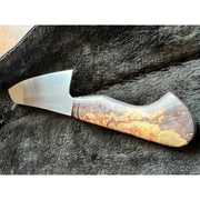 A chef's knife with a satin-finished steel blade and a contoured handle made of swirling brown, gold, and black wood, resting on a dark textured surface.