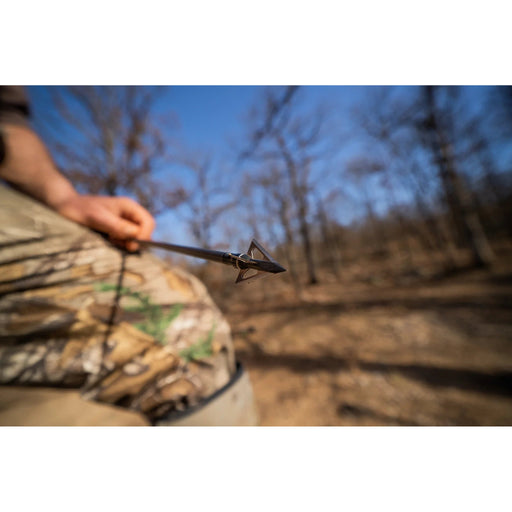 Person in camouflage holding a bow with an arrow in a forest setting