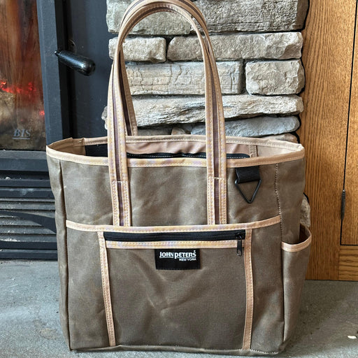 A brown waxed cotton laptop tote with multiple compartments, standing upright on a stone hearth.