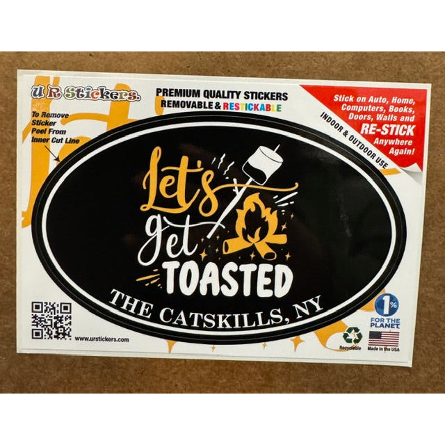 Black, white and yellow sticker with the text "let's get toasted" on a wooden background.