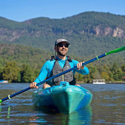 Man paddling a blue kayak on a lake with mountains in the background