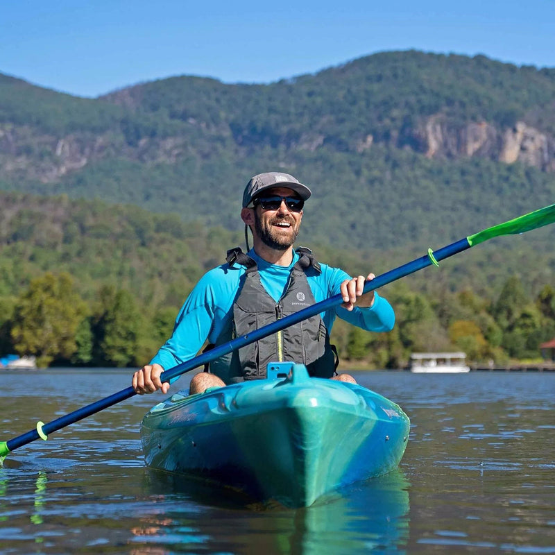 Man paddling a blue kayak on a lake with mountains in the background