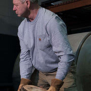 Man wearing a heather gray colored long sleeve shirt with a chest pocket holding a wooden log. The chest pocket has a Carhartt logo on it. 