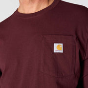 Close up of a man wearing a maroon colored shirt with a chest pocket and a Carhartt logo on a white background. 