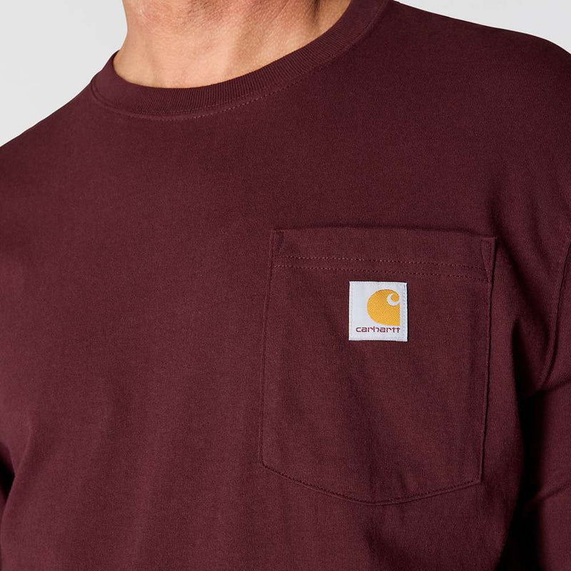 Close up of a man wearing a maroon colored shirt with a chest pocket and a Carhartt logo on a white background. 