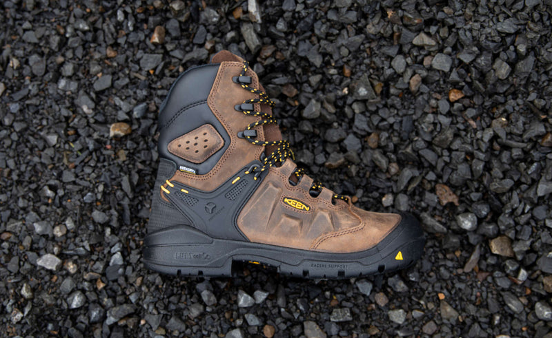 Brown and black work boot with yellow accents laying on a pile of rocks. 
