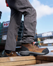 Person wearing a pair of brown and black work boots standing on a pile of lumber. 