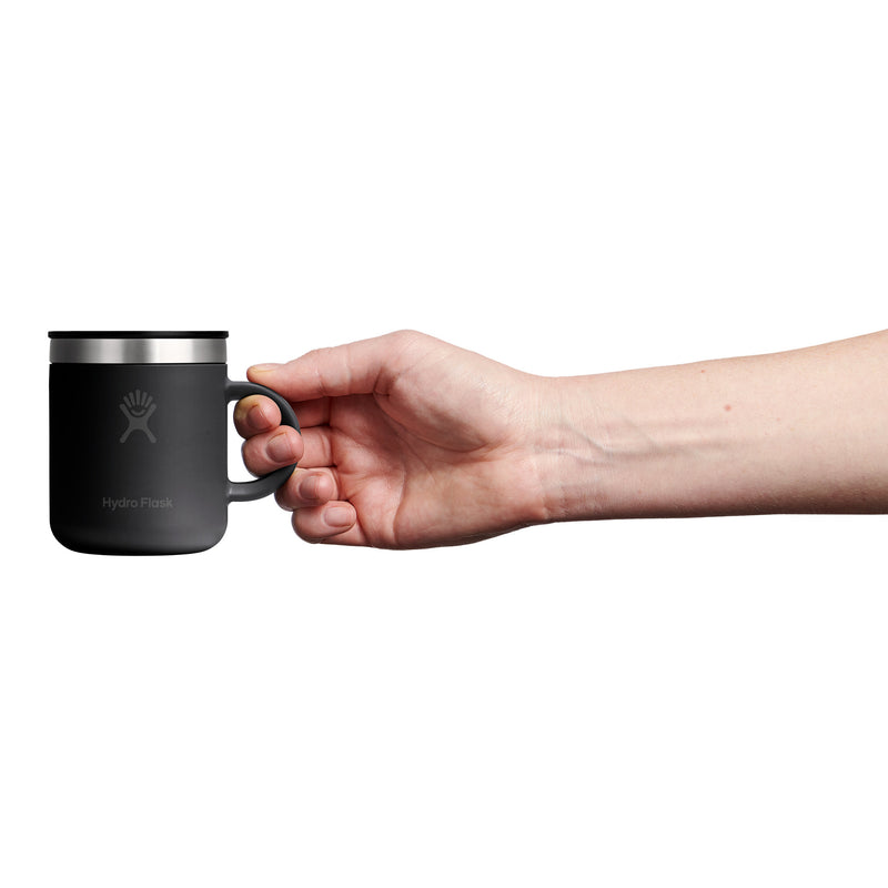 Hand holding a black mug with a silver rim on a white background