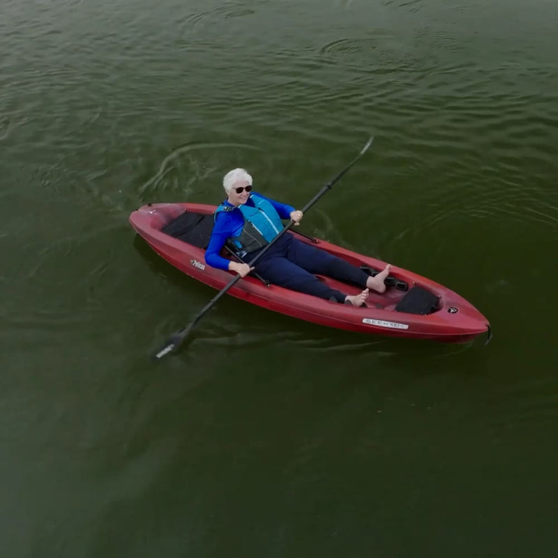 Top view of a smiling woman relaxing in a red kayak in the middle of a lake. 
