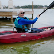 Smiling woman in a red kayak paddling in a lake near a dock. 