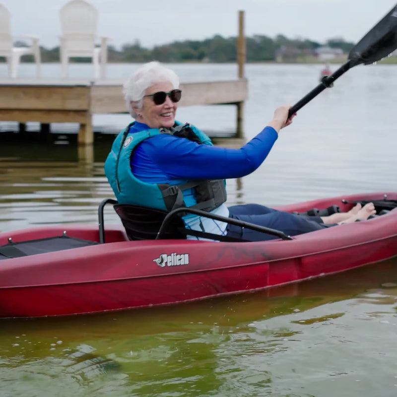 Smiling woman in a red kayak paddling in a lake near a dock. 