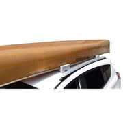 A tan canoe mounted on a white car roof rack, shown against a plain white background.