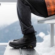 Person wearing black boots with a blurred snowy background