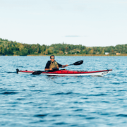 Man paddling a red and white kayak on a calm lake.