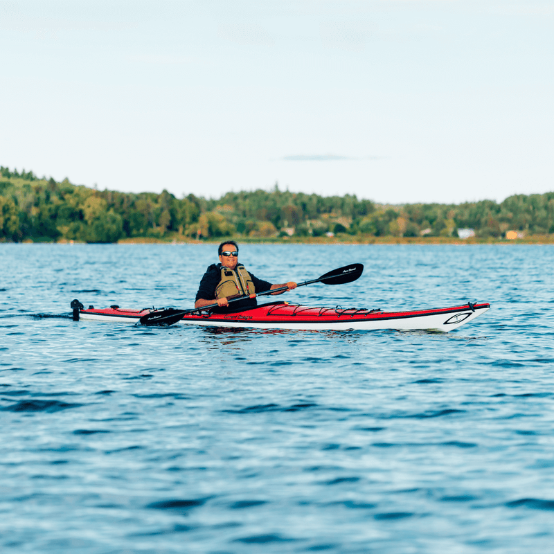 Man paddling a red and white kayak on a calm lake.