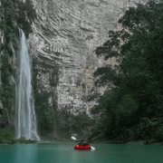 Kayaker in a red kayak paddling towards a waterfall in a lush green forest.