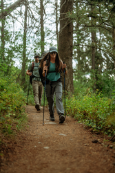 Woman hiking through the woods wearing a pair of grey cargo pants with trees and foliage in the background.