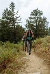 Woman hiking on a trail wearing a pair of grey cargo pants with trees in the background.