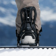 Close up of someone wearing snowboard bindings on their feet against a mountainous background.