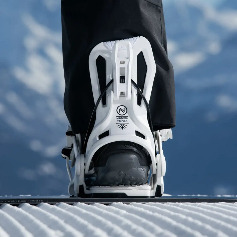 Man standing on a snowboard wearing a white snowboard binding against a sky background. 