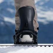 Man standing on a snowboard with his foot in a black binding on a snowy hill. 