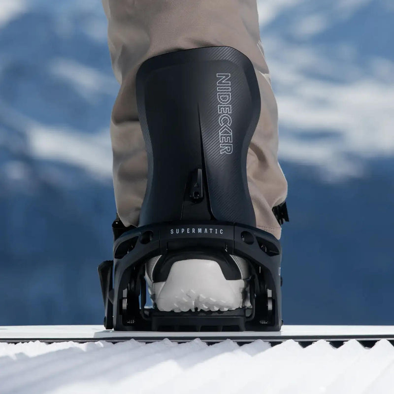 Man standing on a snowboard with his foot in a black binding on a snowy hill. 
