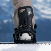 A person standing on a snowboard with their foot in a snowboard binding on a snowy hill. 