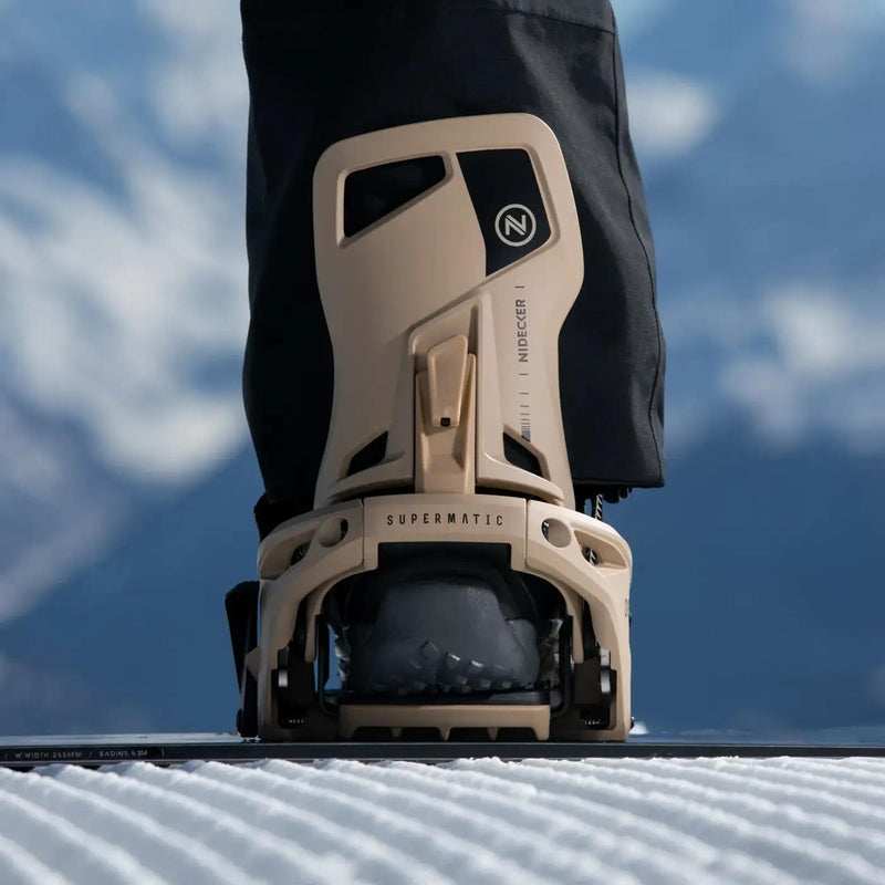 A person standing on a snowboard with their foot in a white colored binding on a snowy mountain. 