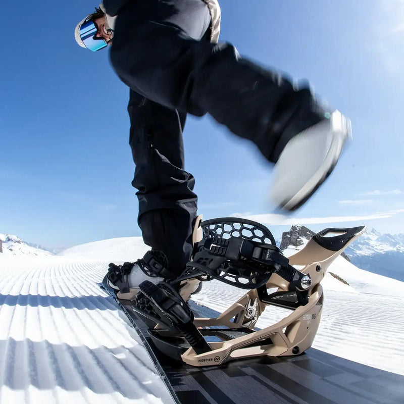 A person putting their foot into a white colored snowboard binding on a snowy hill. 