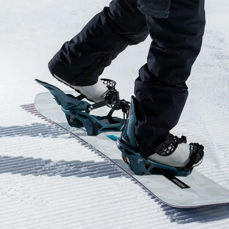 A person with both of their feet in snowboard bindings riding a white snowboard down a snowy hill. 